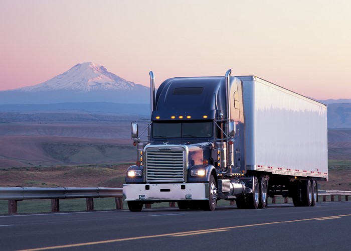 Freightliner semi-truck driving on a highway with a mountain in the background