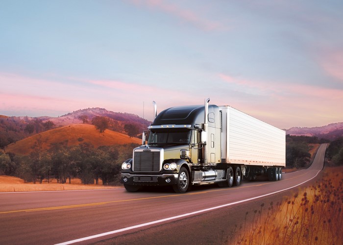 Freightliner semi-truck driving on a road at sunset