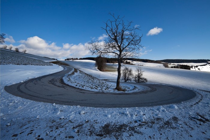 Winding road through snowy landscape with bare tree
