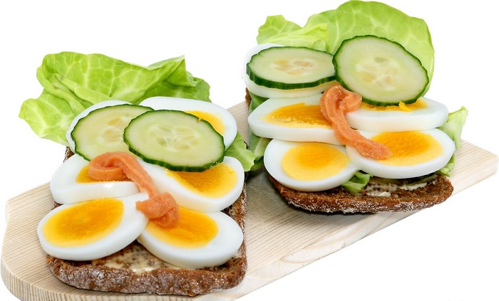 Two open-faced sandwiches with hard-boiled eggs, cucumber, and lettuce