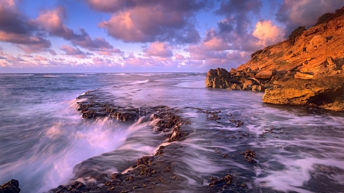 Ocean waves crashing on rocky shore at sunset