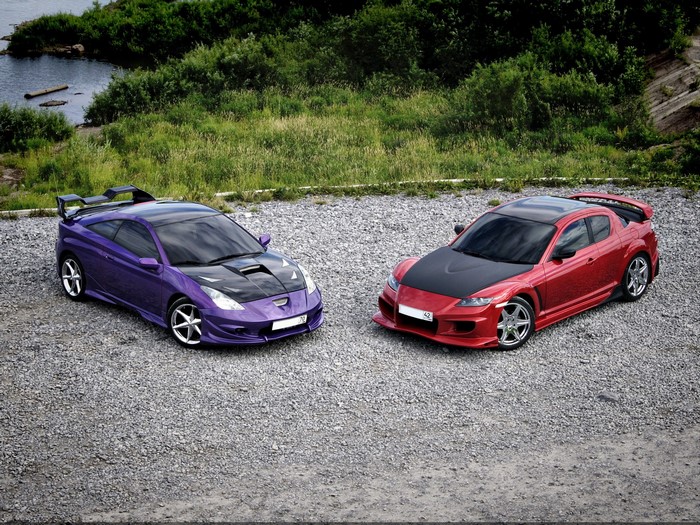 Two modified sports cars, a purple Toyota Celica and a red Mazda RX-8, parked on gravel.