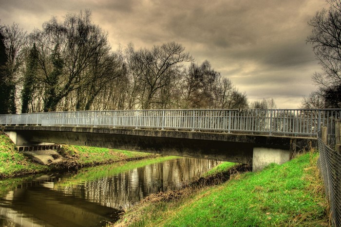Bridge over a canal with trees and cloudy sky