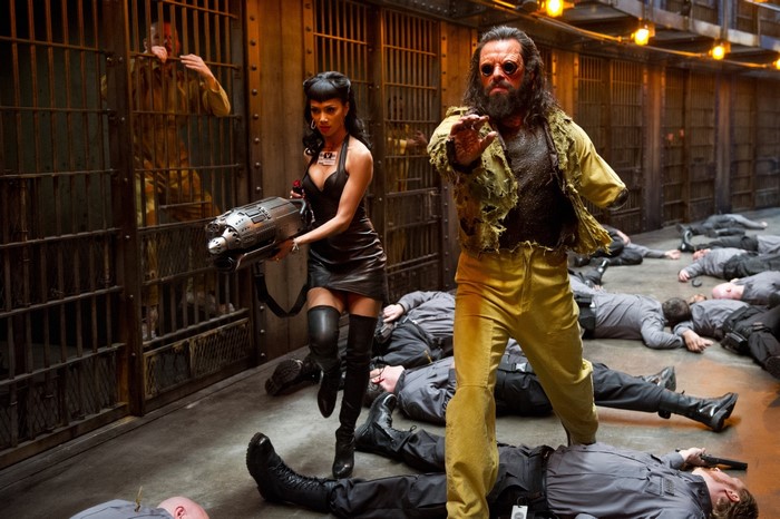 Woman with gun and man with goggles in prison