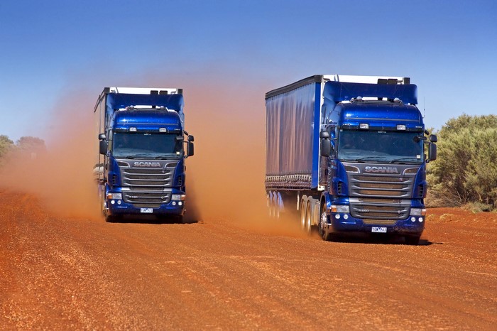 Two blue Scania trucks driving on a dirt road