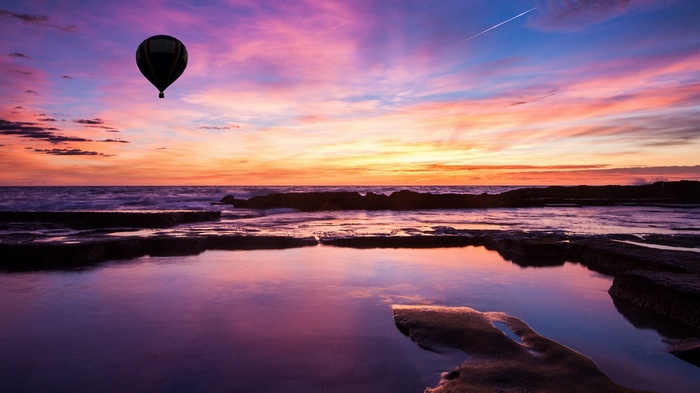 Hot air balloon over ocean at sunset