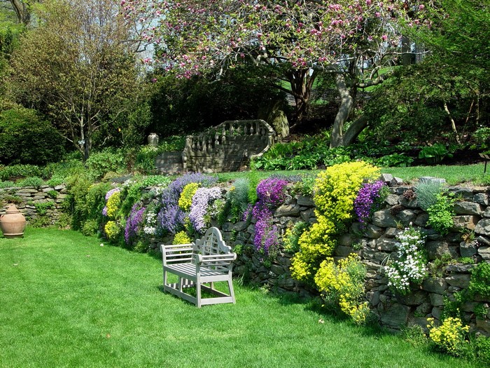 Stone retaining wall with colorful flowers and a bench
