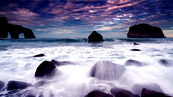 Waves crashing on rocks at sunset with archway