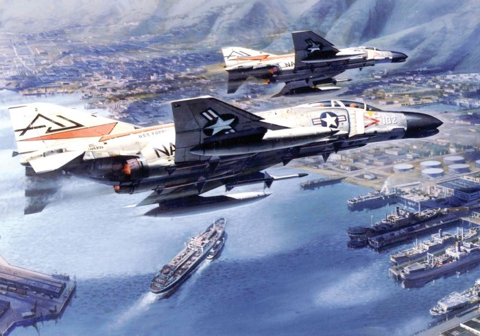 Two US Navy F-4 Phantom II fighter jets flying over a harbor