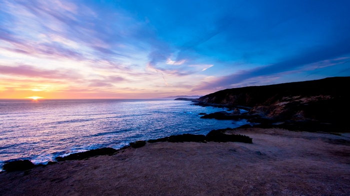 Sunset over the ocean with rocky coastline