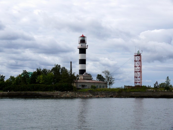 Black and white striped lighthouse and red tower by water
