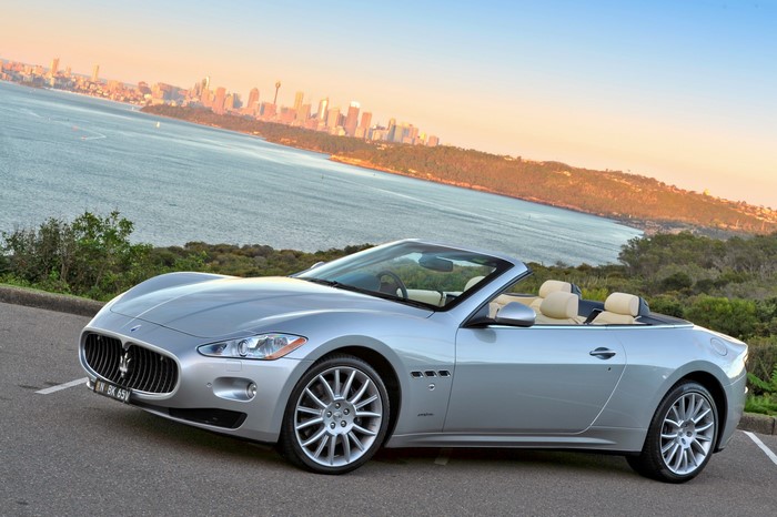 Silver Maserati GranCabrio convertible parked by the water with a city skyline