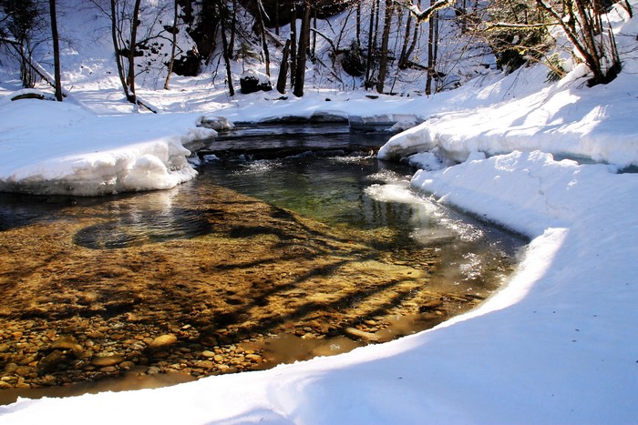 Snowy riverbank with clear water and rocks
