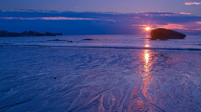 Sunset over the ocean with a large rock