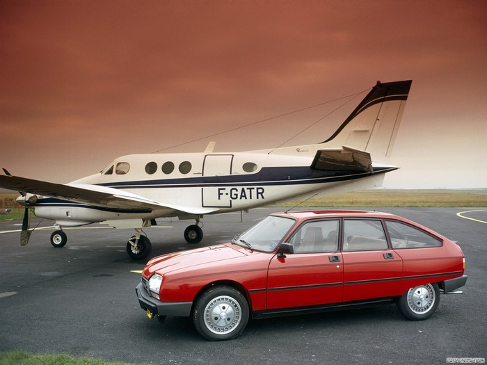 Red Citroen car parked next to a small airplane