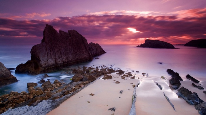 Rocky coastline at sunset with purple clouds