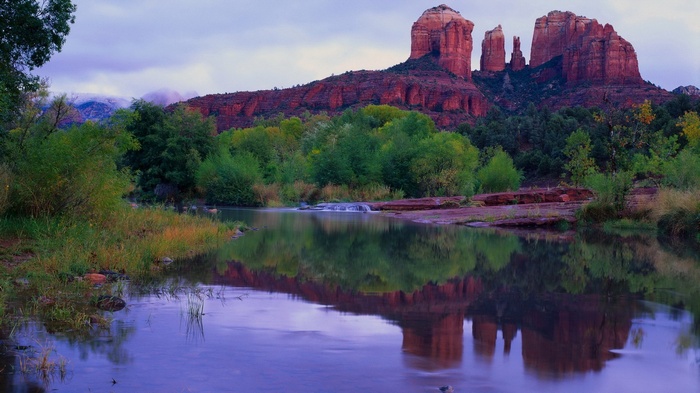 Red rock formations reflected in a calm river with trees