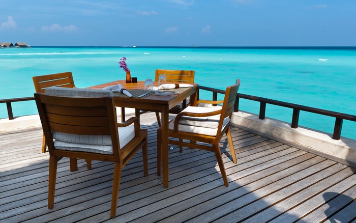 Dining table and chairs on a wooden deck overlooking the ocean