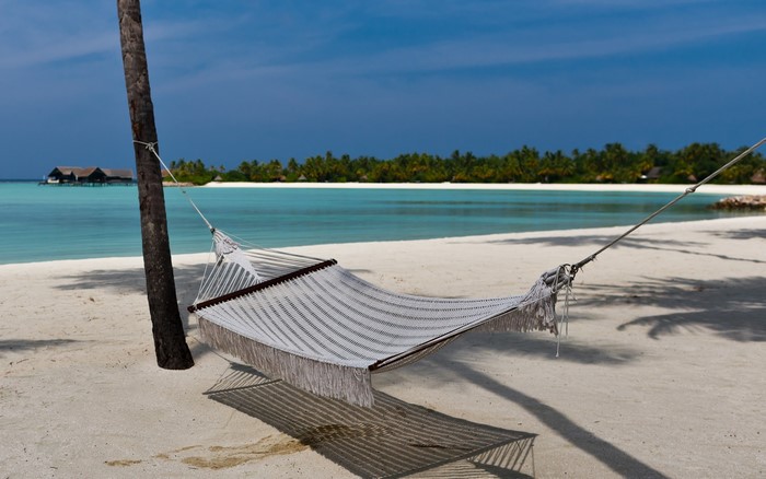 Hammock on a tropical beach with overwater bungalows