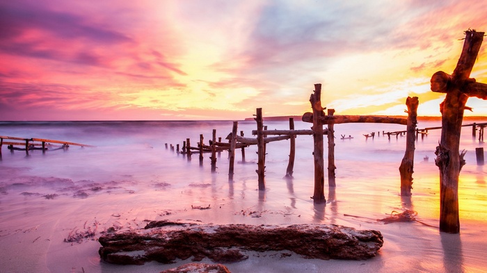 Wooden pier ruins at sunset beach