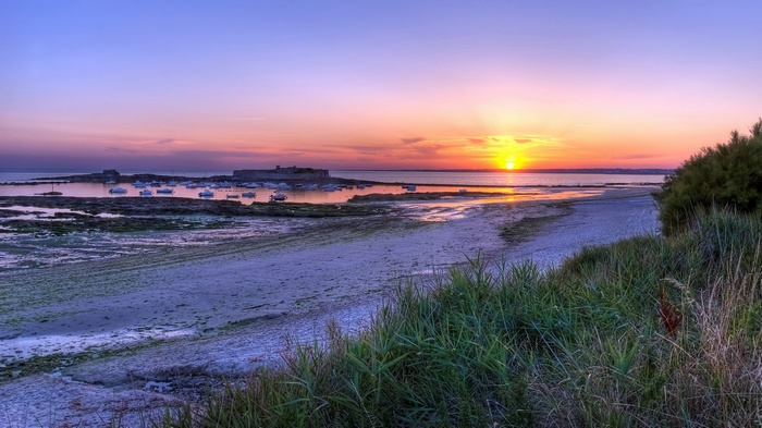 Sunset over a bay with boats and a fort