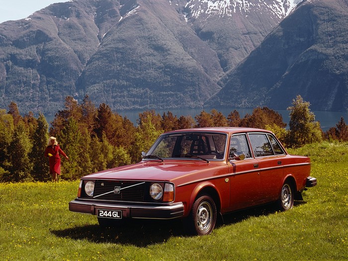 Red Volvo 244 GL parked in a field with a woman