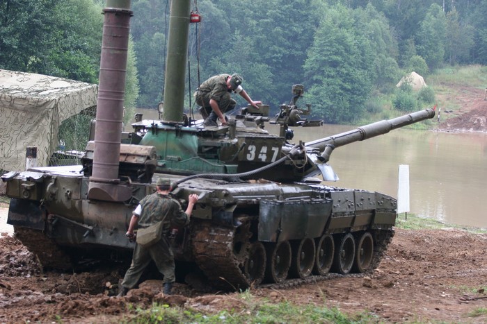 Two soldiers working on a tank near a lake