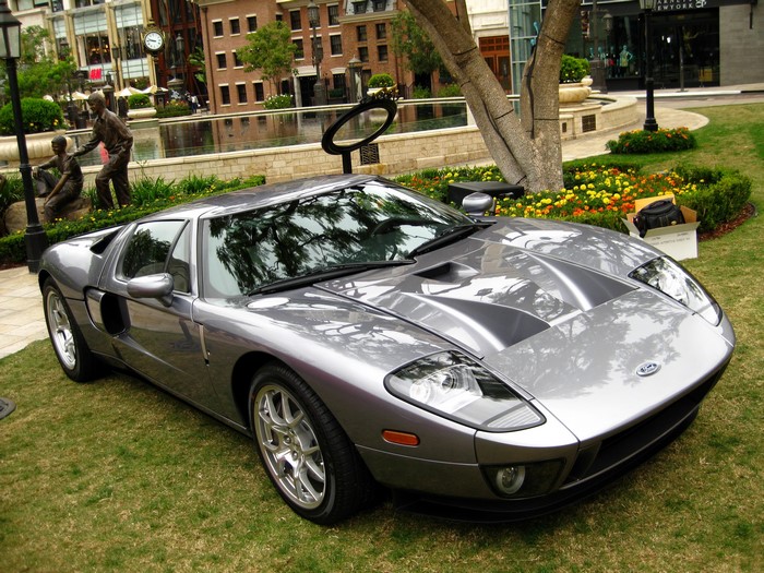 Silver Ford GT parked on grass with buildings in background