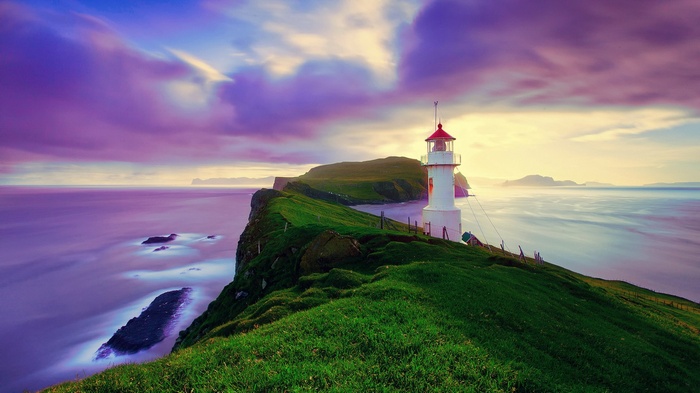 Lighthouse on a grassy cliff overlooking the ocean at sunset