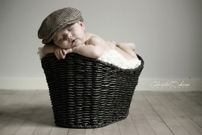Baby sleeping in a wicker basket wearing a cap