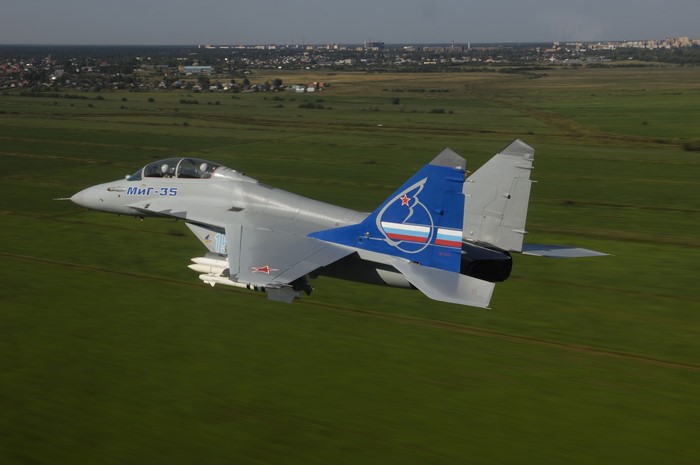 Mikoyan MiG-35 fighter jet flying over green fields