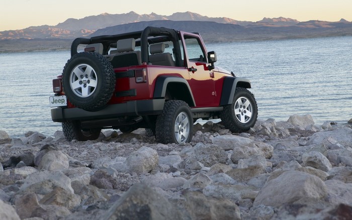 Red Jeep Wrangler parked on rocky shore by lake