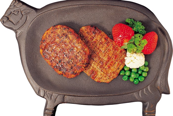 Two grilled patties on a pig-shaped cast iron platter with strawberries and peas