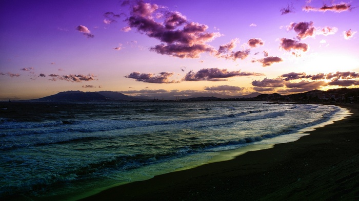Purple sunset over a wavy ocean and a dark beach