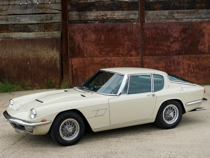 Cream Maserati coupe parked in front of a rustic wall