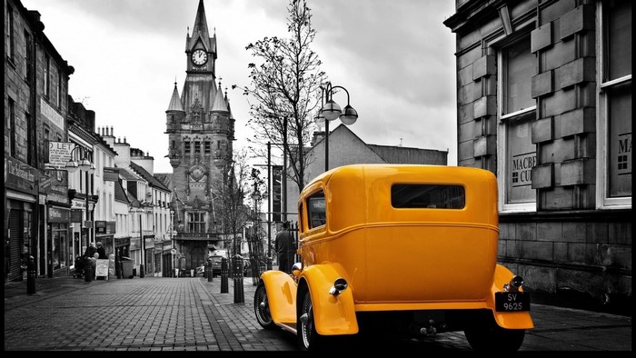 Yellow retro car parked on a cobblestone street with a clock tower