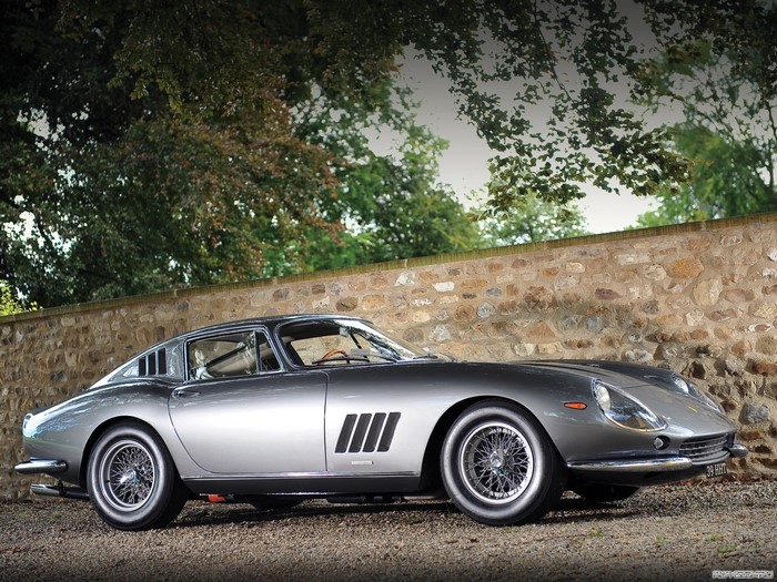 Silver Ferrari 275 GTB/4 parked by a stone wall