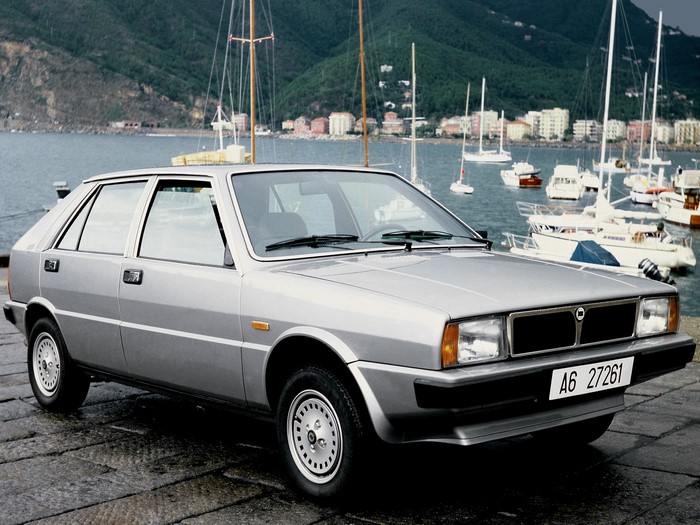 Silver Lancia Delta hatchback parked by a harbor