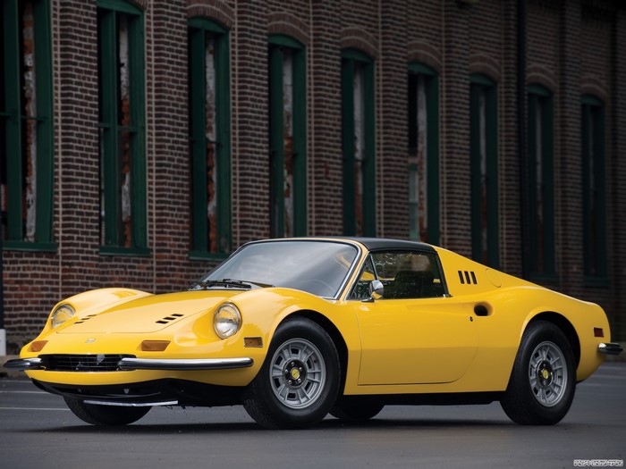Yellow Ferrari Dino 246 GT parked in front of a brick building