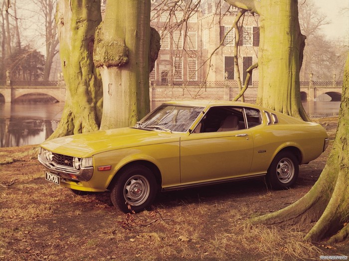 Yellow Toyota Celica parked by trees and a building
