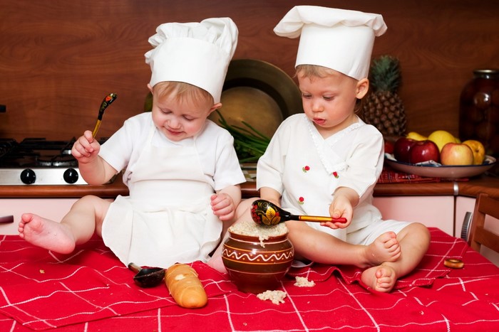 Two baby boys dressed as chefs in a kitchen
