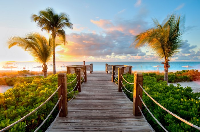 Wooden boardwalk to a tropical beach at sunset