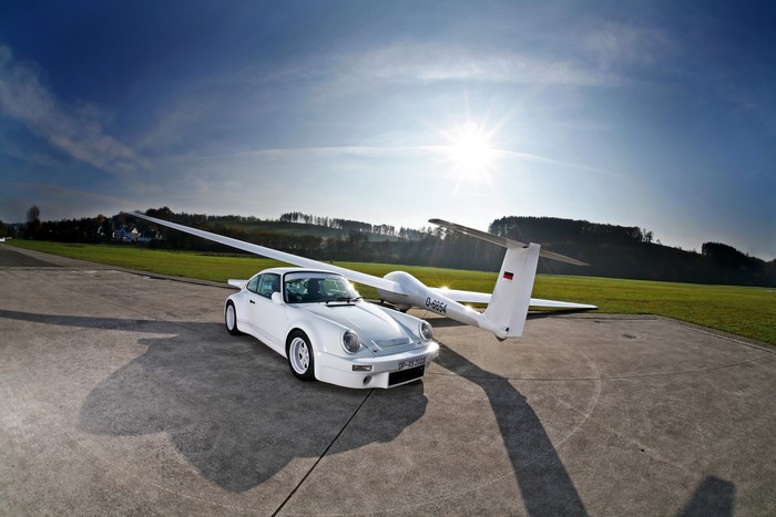 White Porsche 911 next to a glider on an airfield