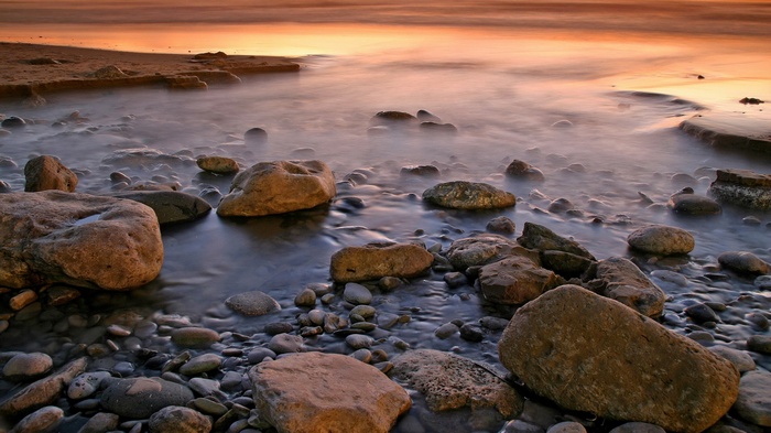 Pebble beach with calm ocean waves at sunset