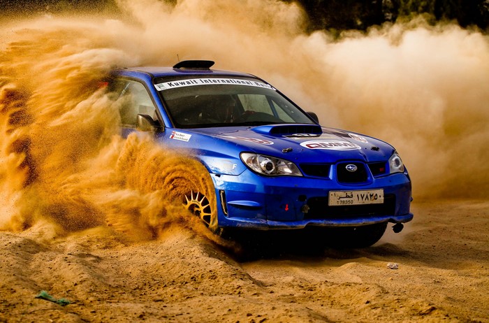 Blue Subaru Impreza rally car kicking up sand