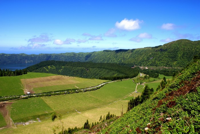 Green rolling hills and a lake under a blue sky