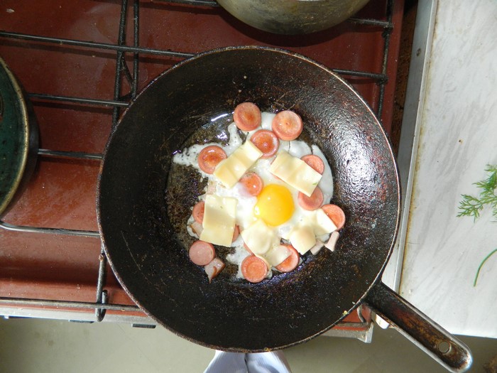Fried egg with sausages and cheese in a frying pan