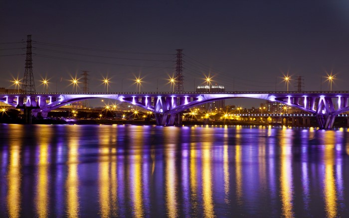 Bridge illuminated with purple lights at night over a river