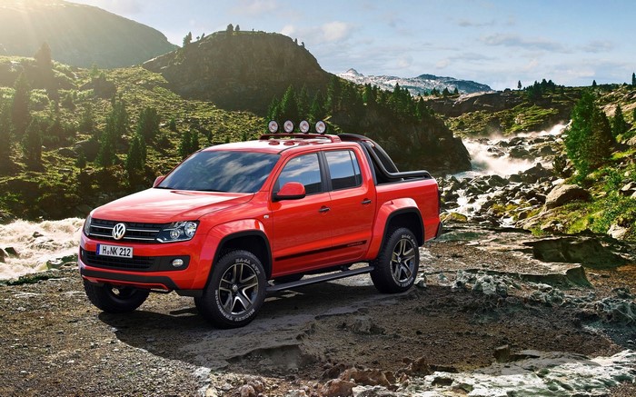 Red Volkswagen Amarok pickup truck in a rocky, mountainous landscape