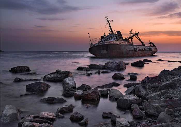 Shipwreck on a rocky shore at sunset